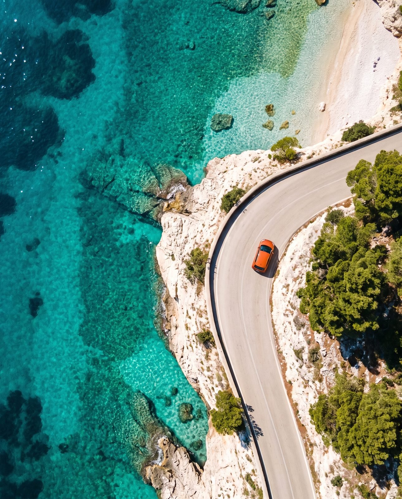 An orange car on a coastal road above turquoise sea